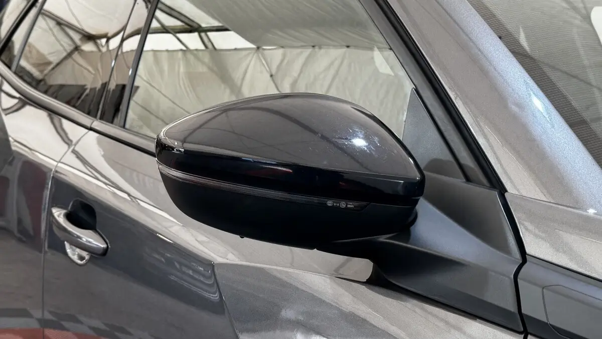 Gros plan sur le rétroviseur droit noir brillant du Peugeot 2008 gris foncé, avec poignée de porte visible.