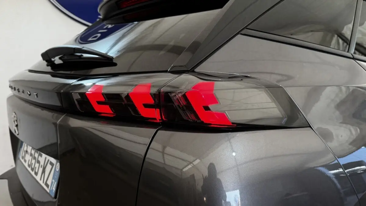Gros plan sur le feu arrière droit rouge vif d’un Peugeot 2008 gris foncé, avec reflet sur la carrosserie lisse.