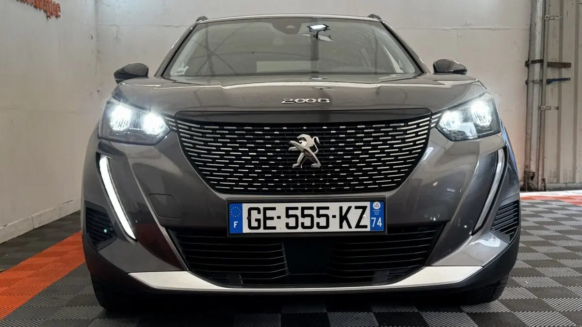 Vue frontale d'un Peugeot 2008 gris foncé 2022 avec phares LED allumés et calandre à motifs chromés.
