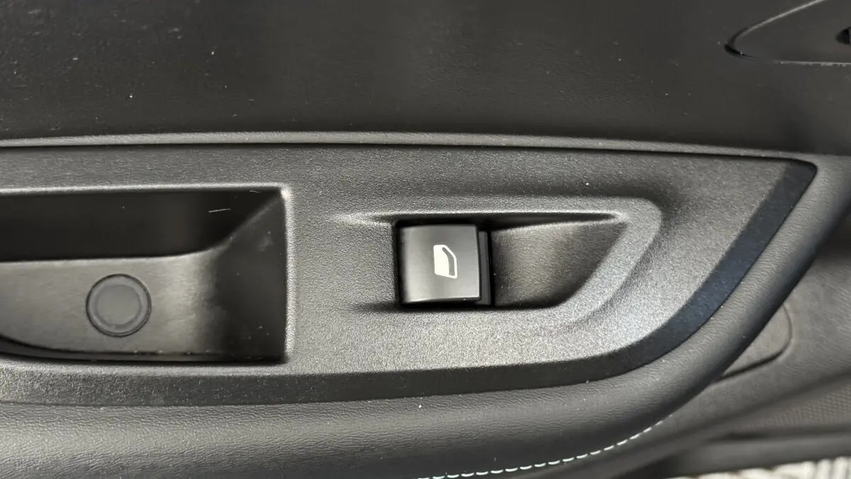 Bouton de commande de vitre électrique sur la porte intérieure noire d'un Peugeot 2008 gris foncé, vue rapprochée.