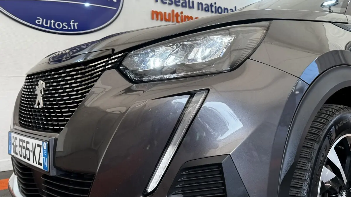 Gros plan sur l'avant droit gris foncé du Peugeot 2008 2022, mettant en valeur le phare LED et la calandre distinctive.
