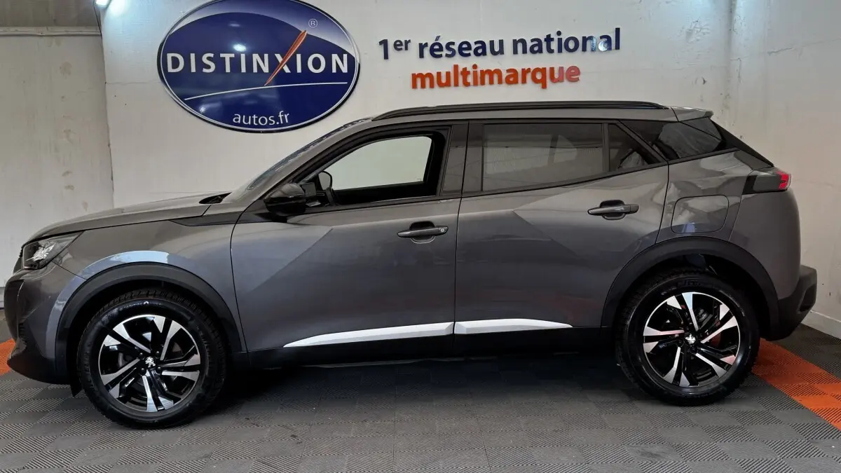 Profil côté gauche du Peugeot 2008 gris foncé 2022 avec jantes alliage bicolores et toit noir contrasté.