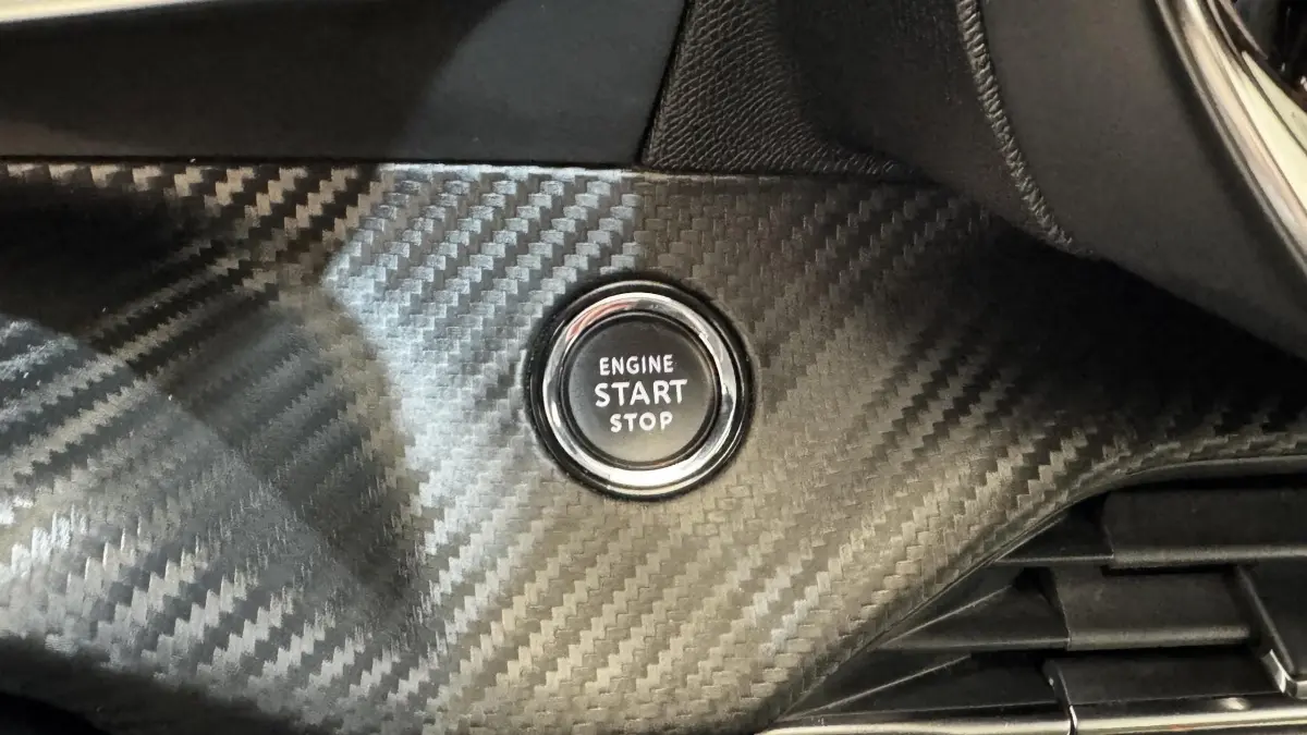 Gros plan sur le bouton start/stop moteur entouré d’un habillage carbone à l’intérieur du Peugeot 2008 gris foncé.