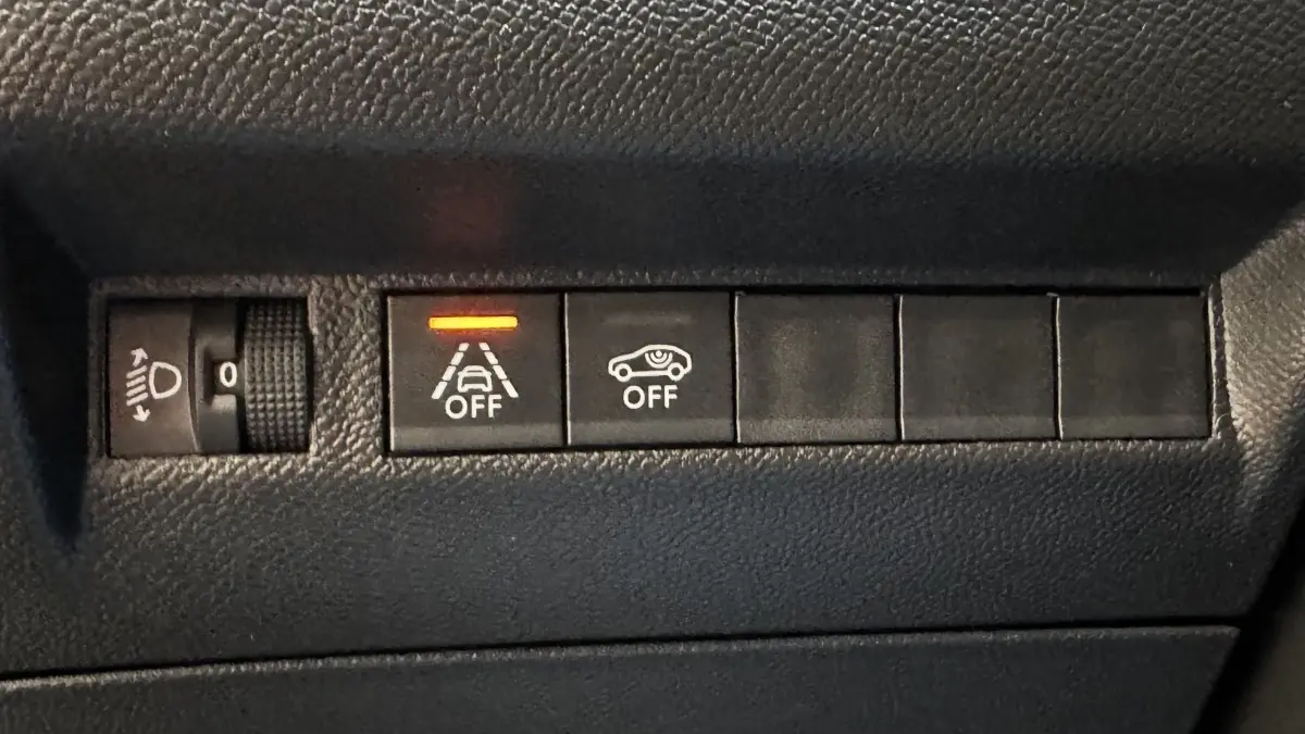 Gros plan sur les boutons de commande du tableau de bord du Peugeot 2008 gris foncé, avec témoin orange allumé.