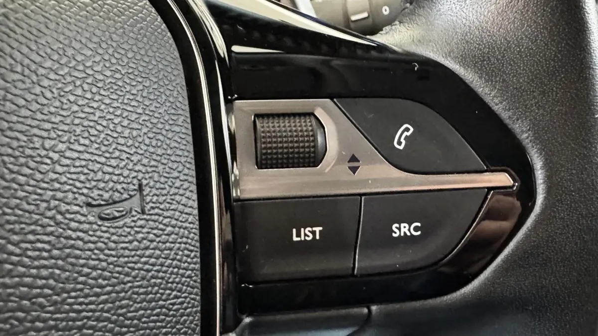 Gros plan sur les commandes multifonctions noires du volant cuir d’un Peugeot 2008 gris foncé, version 2022.