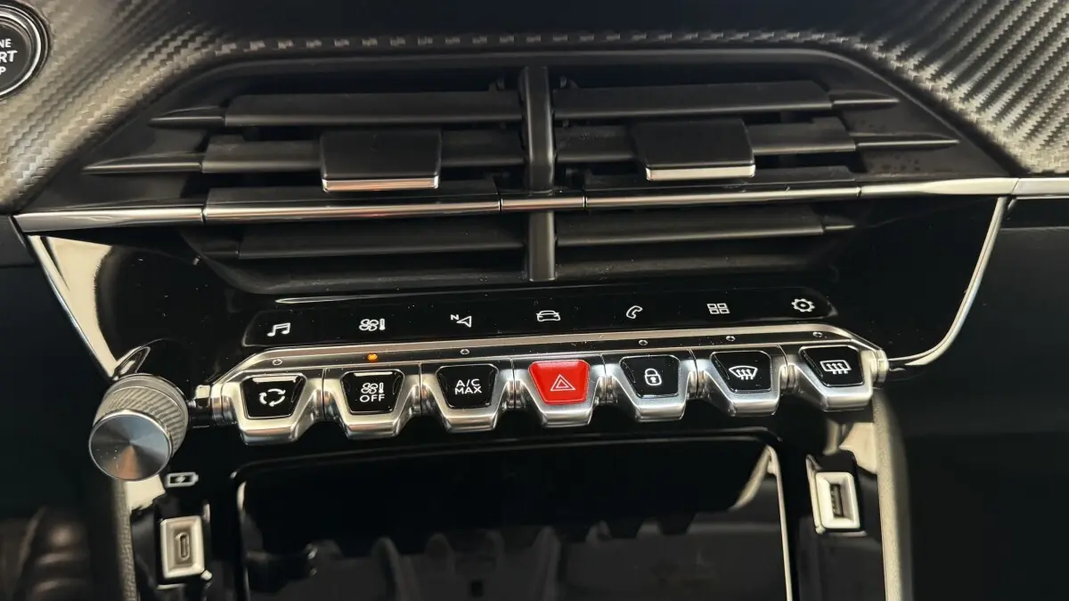 Gros plan sur la console centrale de la Peugeot 2008 gris foncé, mettant en valeur les boutons chromés et l'aération noire.