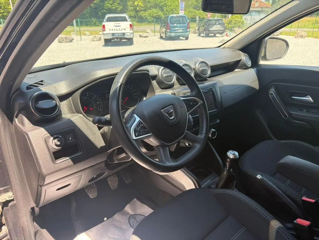 Vue intérieure côté conducteur du Dacia Duster gris 2021, montrant le volant, tableau de bord et levier de vitesses manuel.