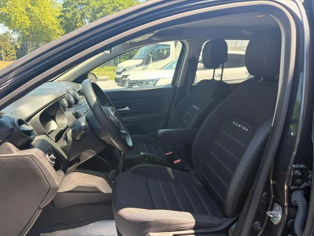Vue intérieure côté conducteur du Dacia Duster gris 2021, avec sièges noirs marqués "DUSTER" et tableau de bord simple.
