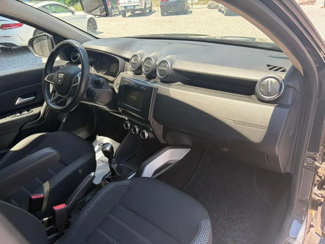 Vue intérieure côté conducteur du Dacia Duster gris 2021, mettant en valeur le tableau de bord et la boîte manuelle.