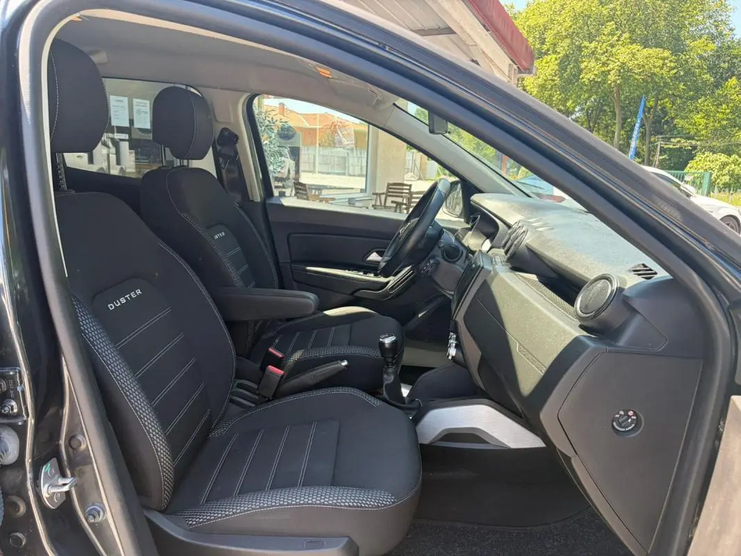 Vue intérieure côté conducteur du Dacia Duster gris 2021, sièges noirs avec logo Duster et levier de vitesses manuel visible.