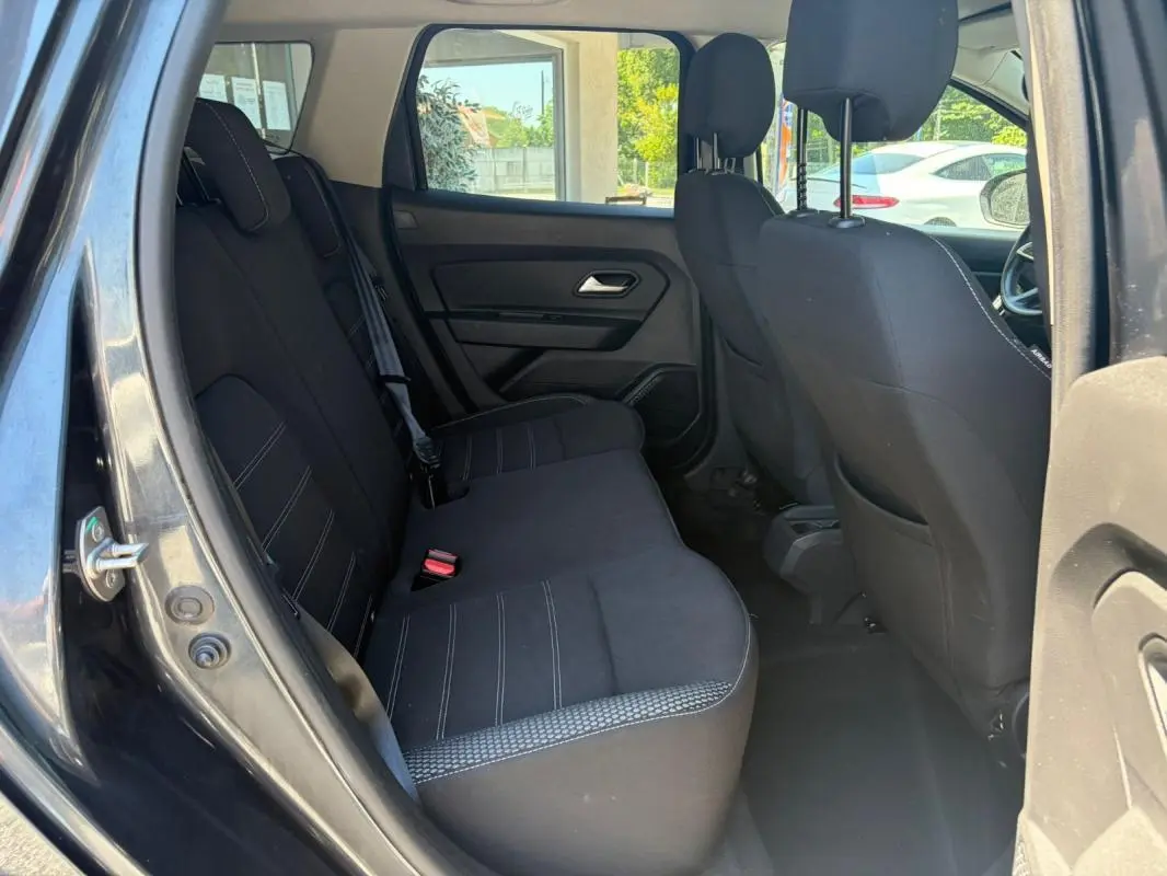 Vue intérieure côté arrière gauche du Dacia Duster gris 2021, montrant les sièges arrière en tissu noir avec surpiqûres blanches.