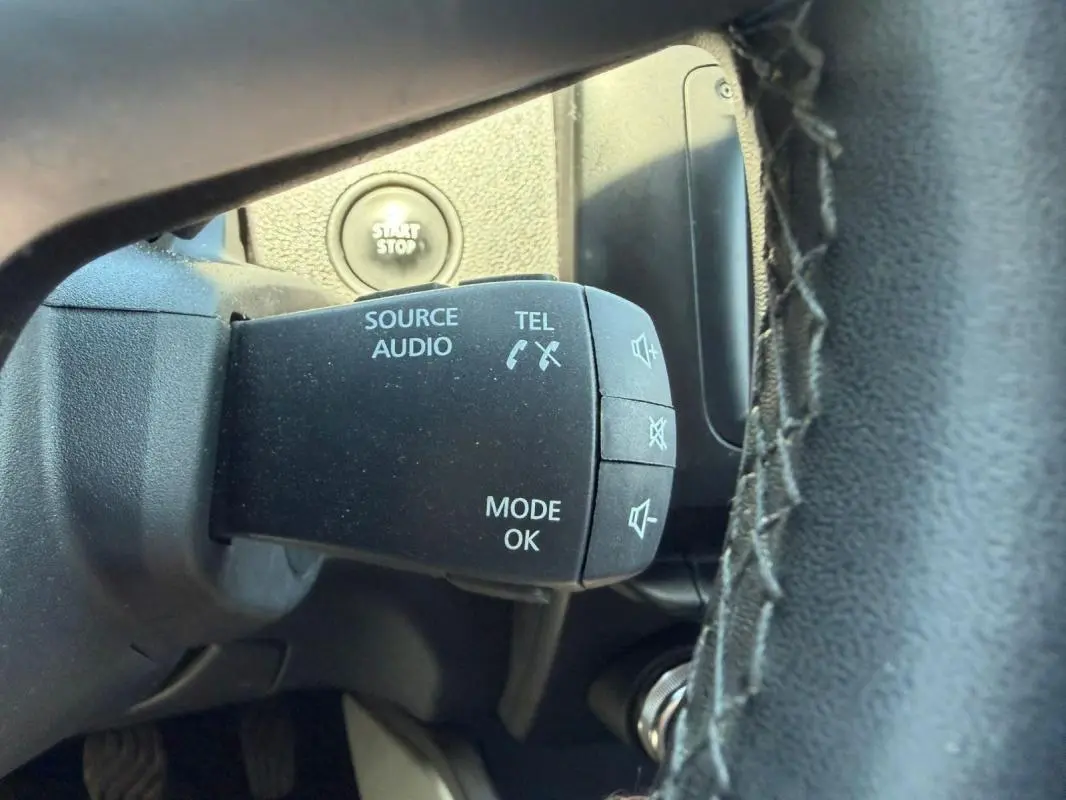 Gros plan sur la commande audio au volant du Dacia Duster gris, avec bouton start/stop visible en arrière-plan.