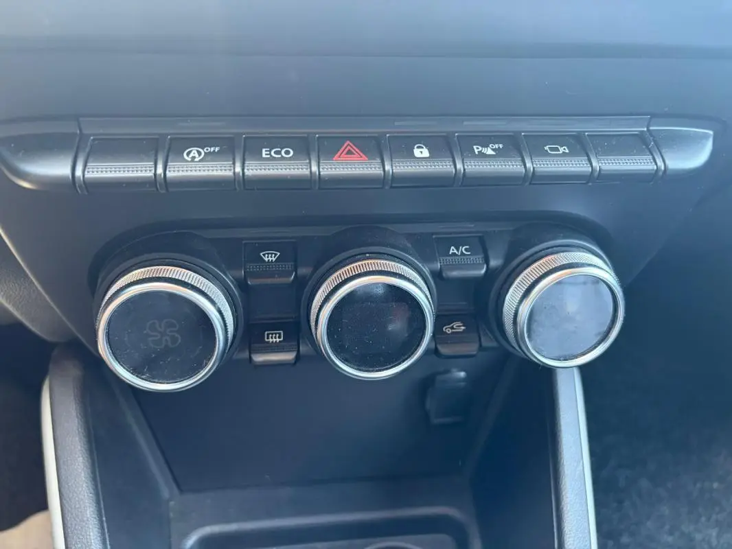 Tableau de bord du Dacia Duster 2021, vue rapprochée des commandes de climatisation et des boutons fonctionnels noirs.