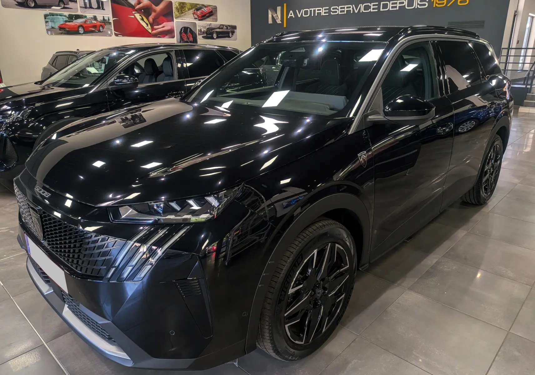 Peugeot 5008 Hybrid 145 GT noir Perla, vue 3/4 avant droit, avec jantes biton et calandre distinctive en showroom.