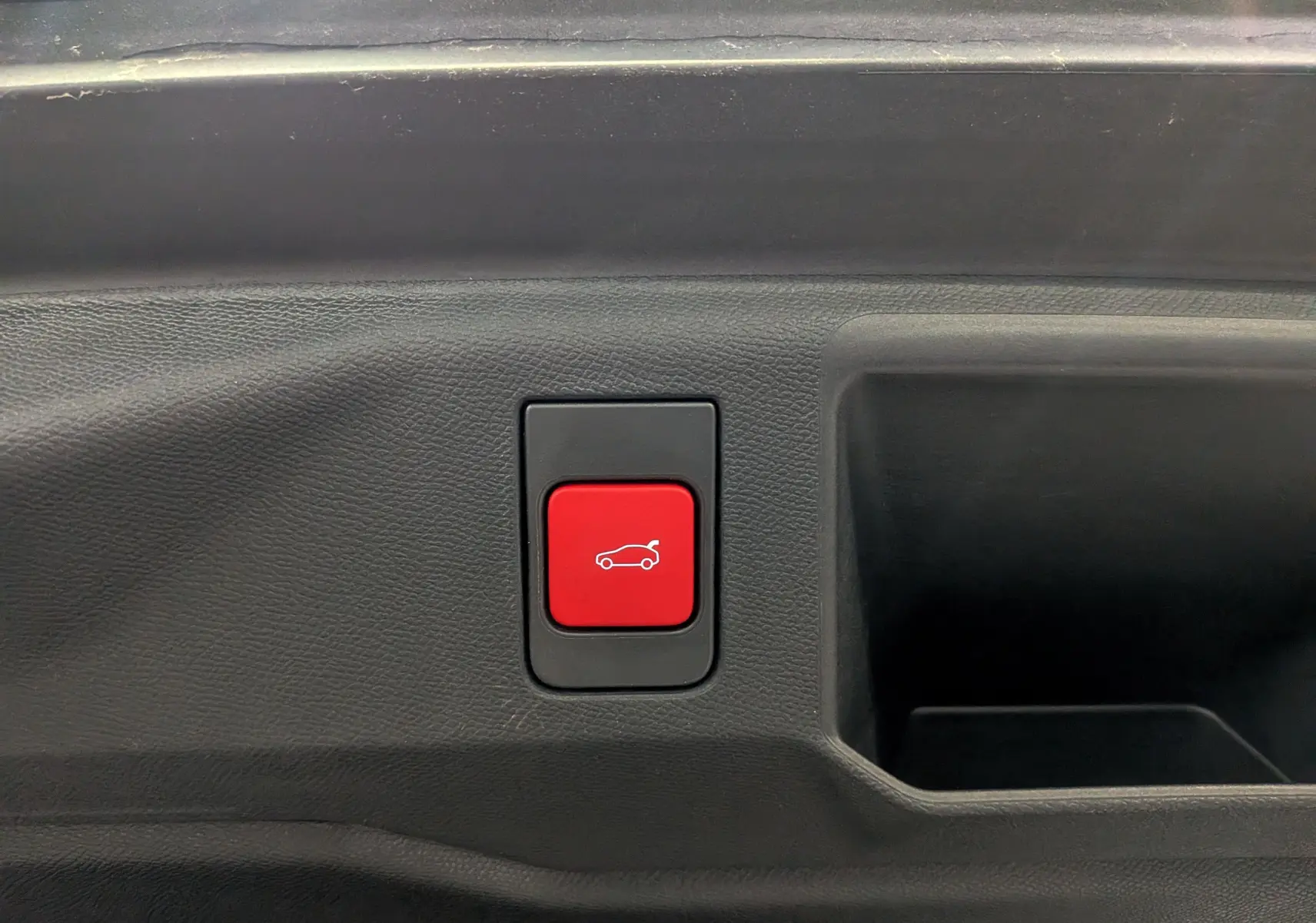 Bouton rouge d'ouverture électrique du hayon sur panneau intérieur noir d'un Peugeot 5008 Hybrid 2025.