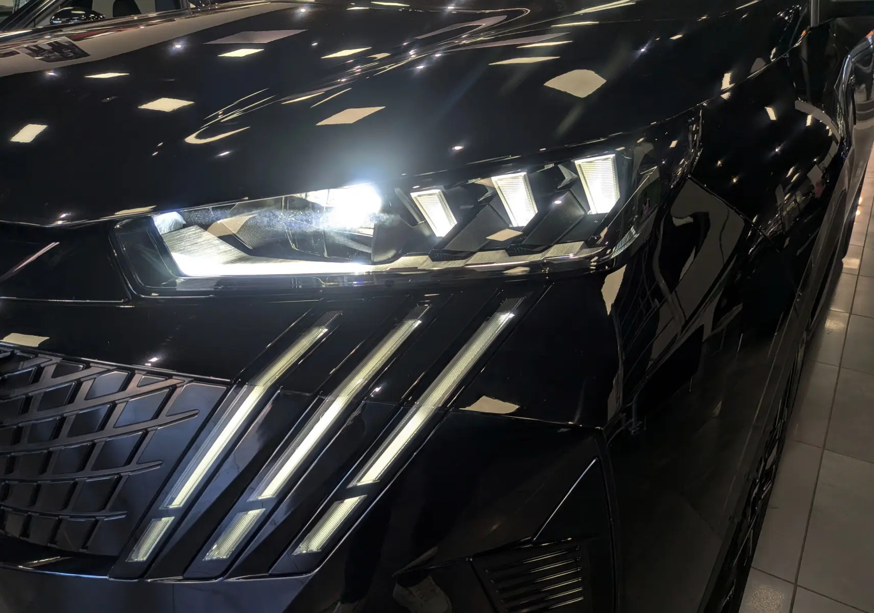 Gros plan sur le phare avant droit allumé du Peugeot 5008 Hybrid noir Perla, soulignant les LED distinctives en griffes.
