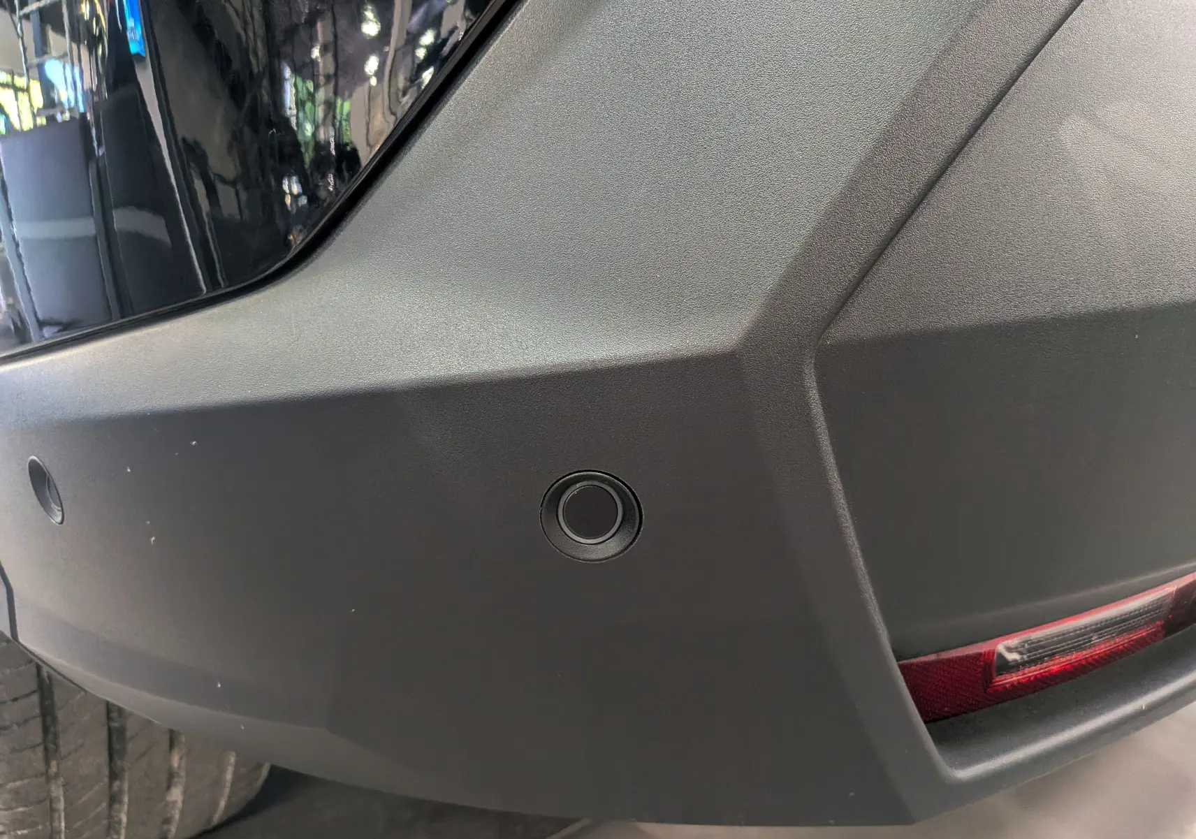 Gros plan sur le pare-chocs arrière noir Perla du Peugeot 5008 Hybrid 145 CH e-DCS6 GT avec capteur de recul visible.