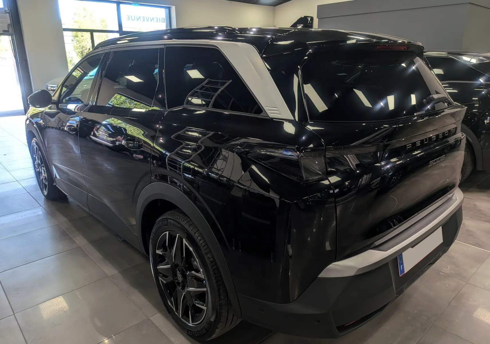 Peugeot 5008 HYBRID 145 GT noir Perla vue 3/4 arrière droit en intérieur, avec jantes biton et toit noir brillant.