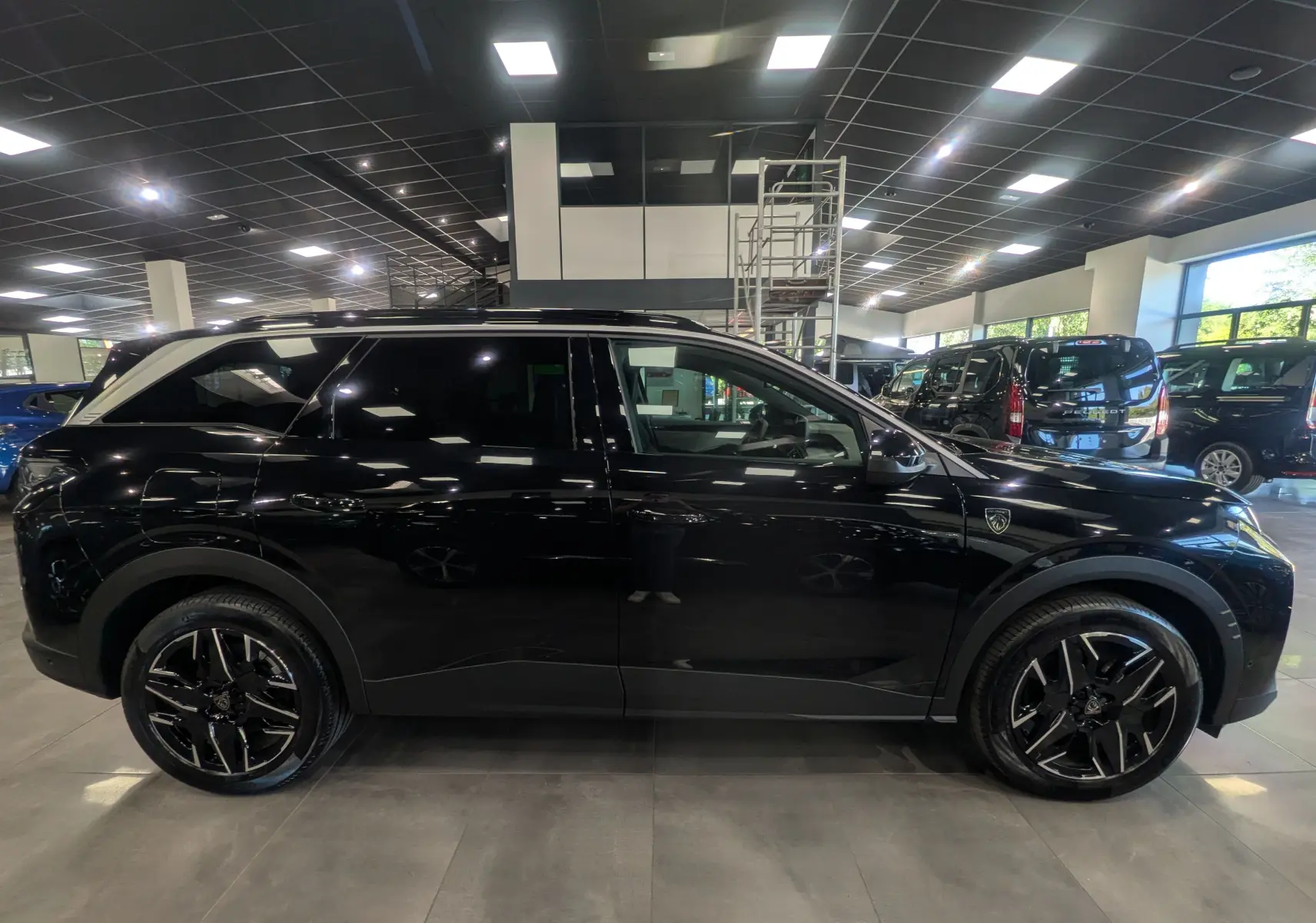 Profil latéral droit du Peugeot 5008 Hybrid 145 GT noir Perla, avec jantes noires et toit panoramique en showroom.