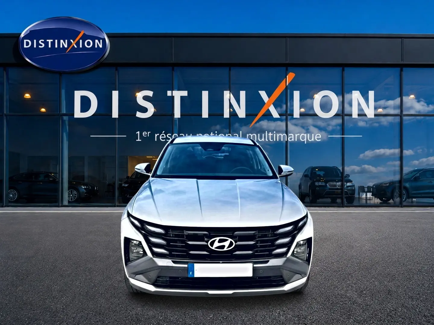 Vue frontale d'un Hyundai Tucson blanc 2026 hybride devant une vitrine avec logo Distinxion.
