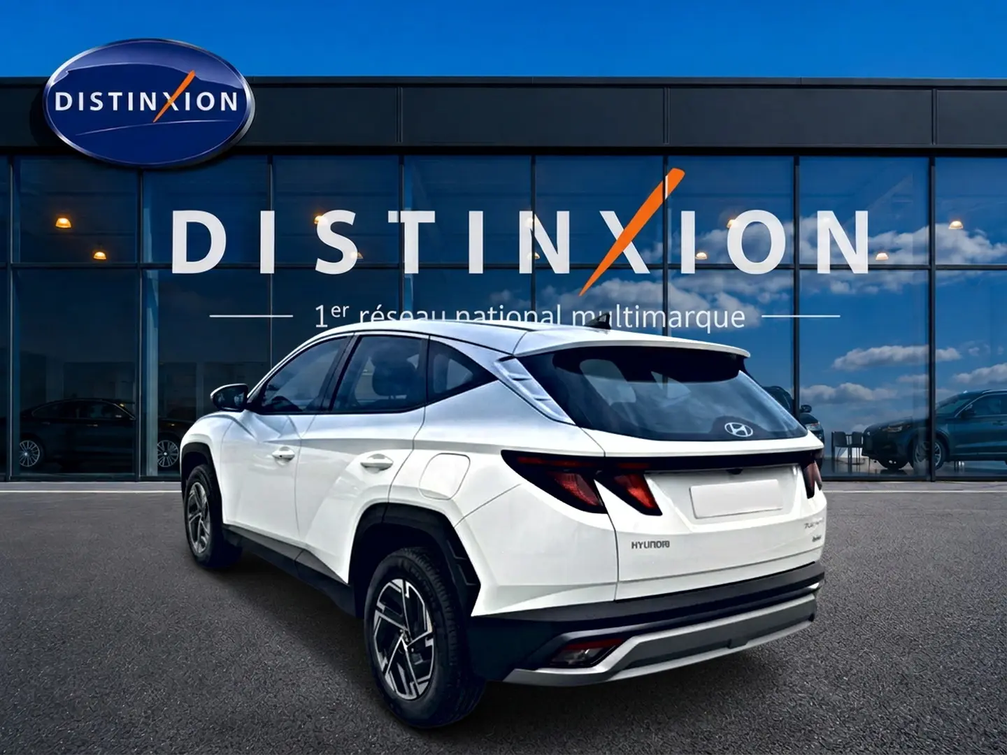 Vue 3/4 arrière droite du Hyundai Tucson blanc hybride 2026 avec jantes alliage et feux arrière LED, devant un showroom Distinxion.