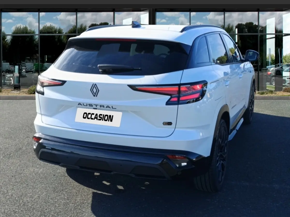 Vue 3/4 arrière droite d'un Renault Austral blanc avec feux arrière LED et logo central sur fond urbain.