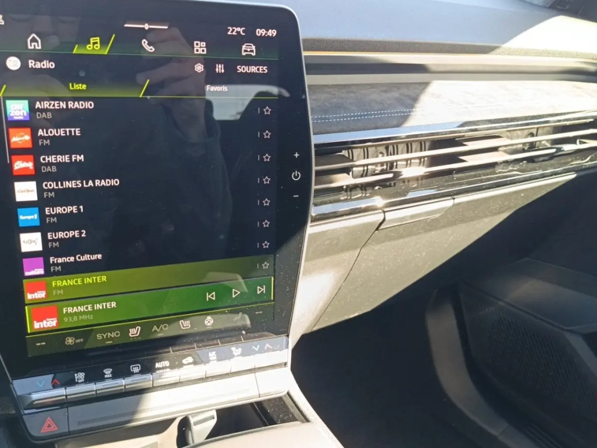 Intérieur du Renault Austral esprit Alpine blanc, vue sur l'écran tactile central et la planche de bord avec finition noire et surpiqûres bleues.