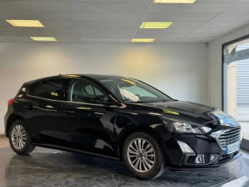 Ford Focus noir Agate métallisé vue 3/4 avant droit en intérieur avec calandre chromée et phares LED.