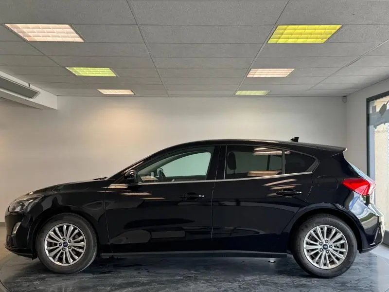 Profil côté gauche de la Ford Focus Titanium X Business noire Agate métallisé, en intérieur avec jantes alliage visibles.