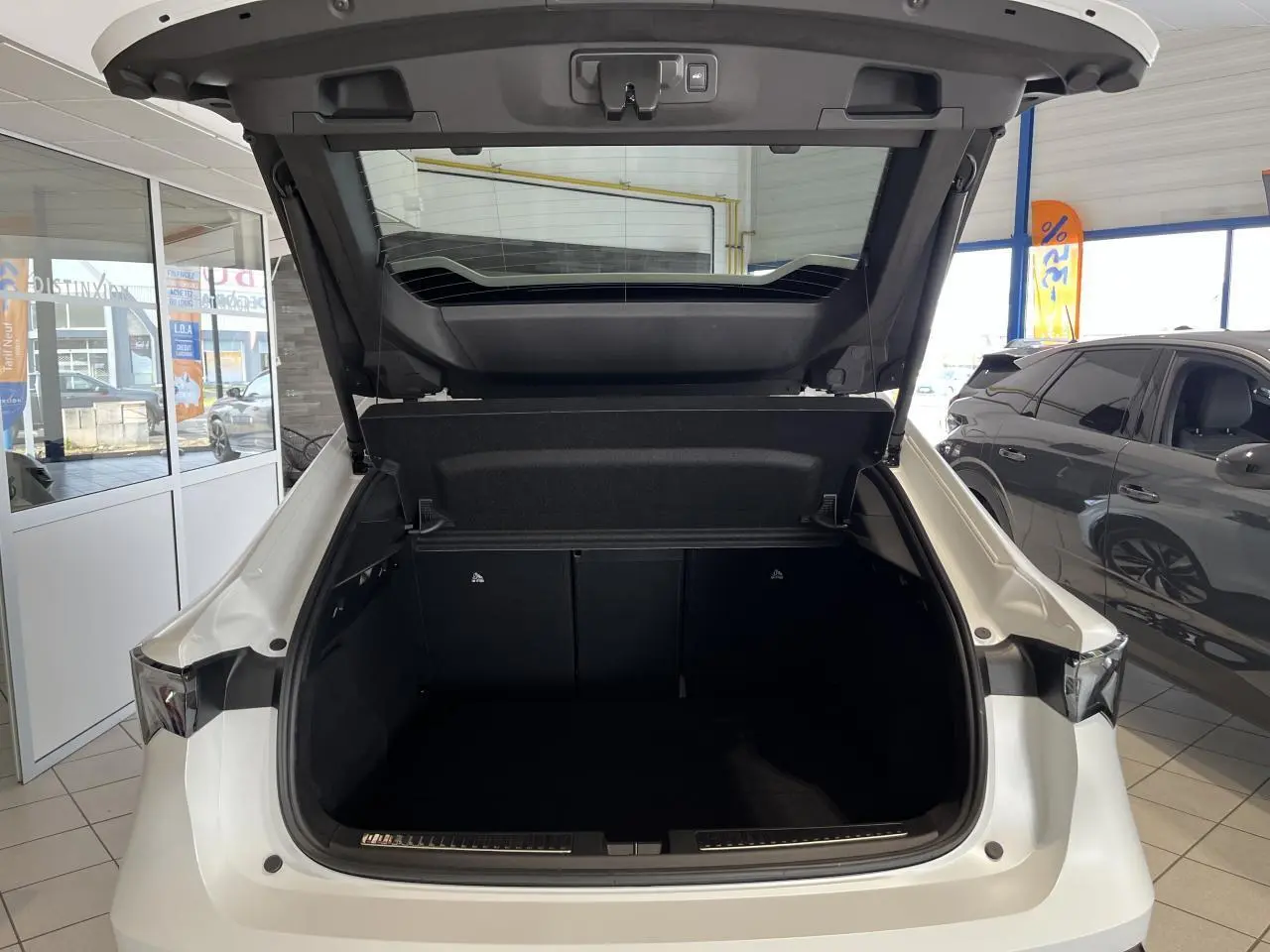 Coffre ouvert vu de l'arrière d'une Renault Rafale blanche 2025 en showroom, avec hayon motorisé visible.