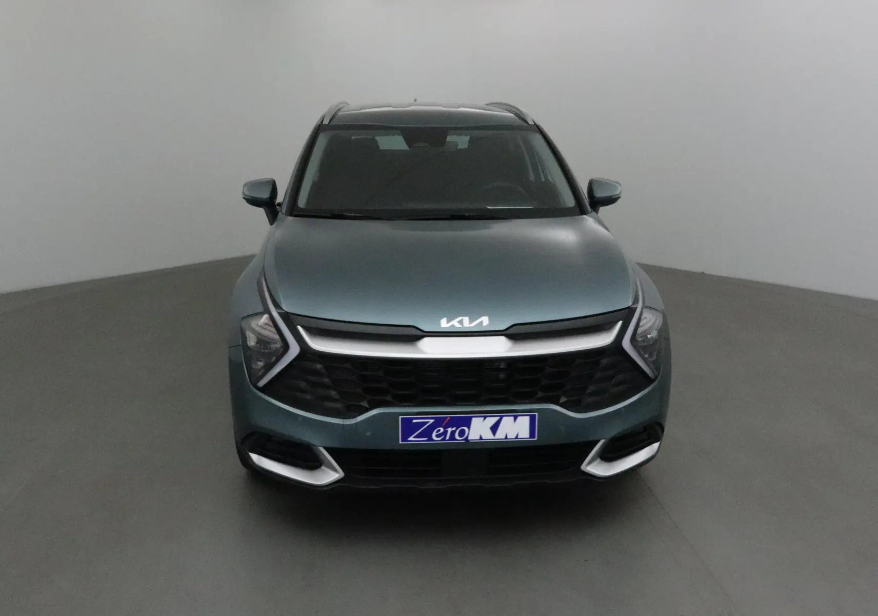 Vue frontale d'un KIA Sportage gris Sirius 2025 avec calandre noire et logo KIA lumineux sur capot.
