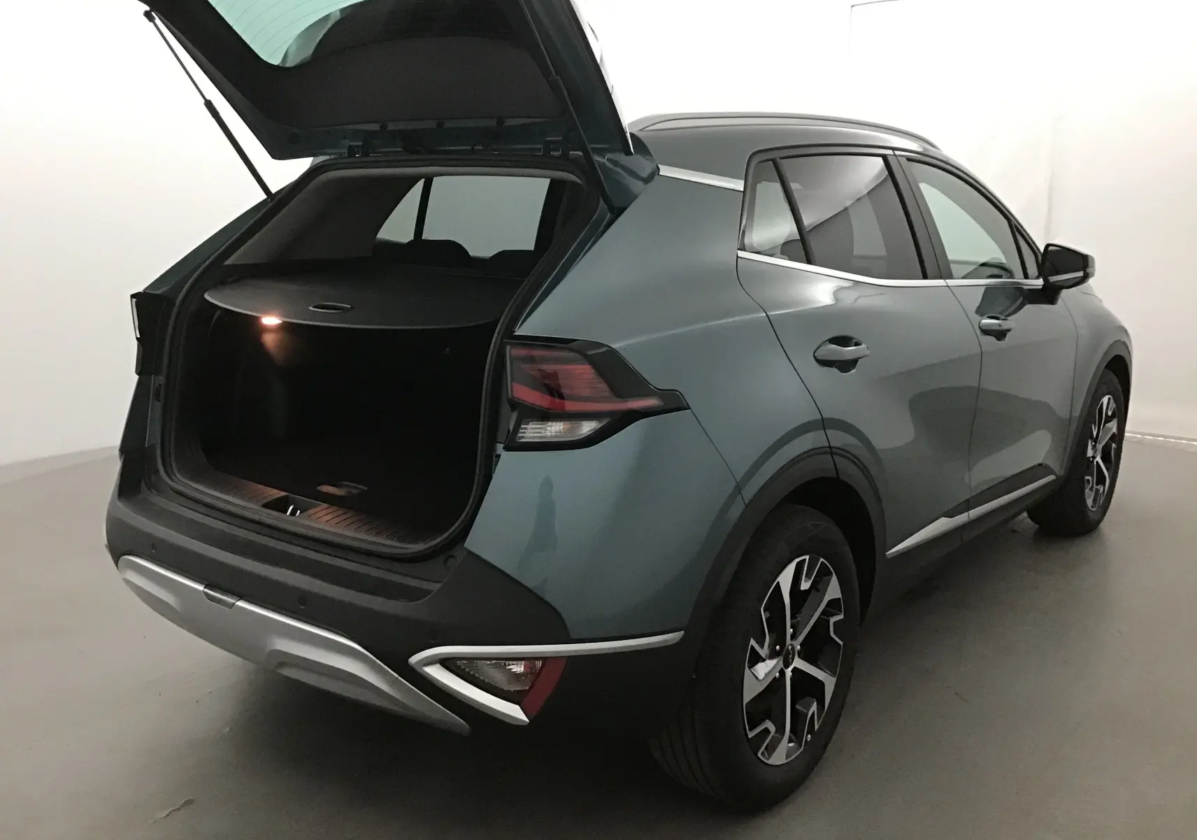 KIA SPORTAGE gris Sirius vu 3/4 arrière droit avec coffre ouvert et feux arrière LED allumés.