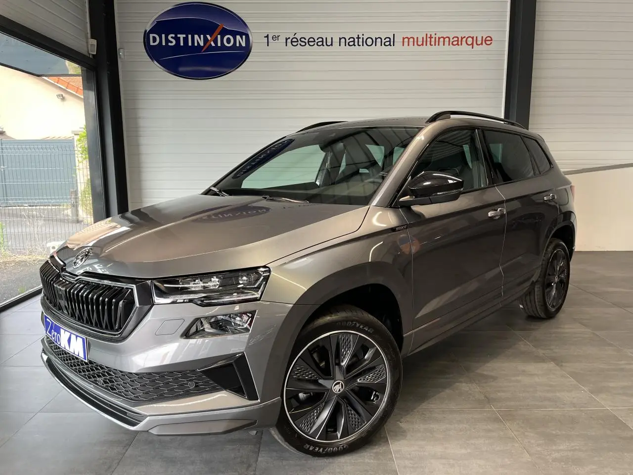 Vue 3/4 avant droite d'un SUV SKODA KAROQ gris métallisé avec jantes alliage noires et calandre noire sportive.
