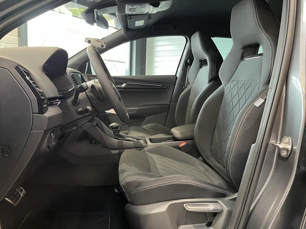 Vue intérieure côté conducteur du Skoda Karoq gris 2025, mettant en valeur les sièges sport noirs et le tableau de bord moderne.