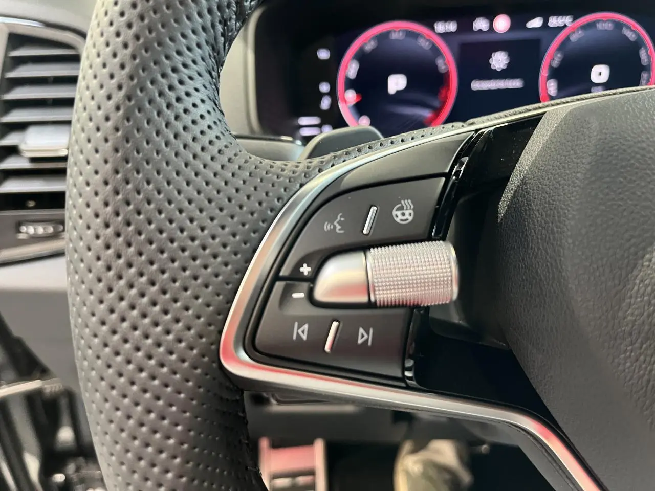 Gros plan sur les commandes gauche du volant perforé noir du Skoda Karoq 2025 avec tableau de bord digital en arrière-plan.