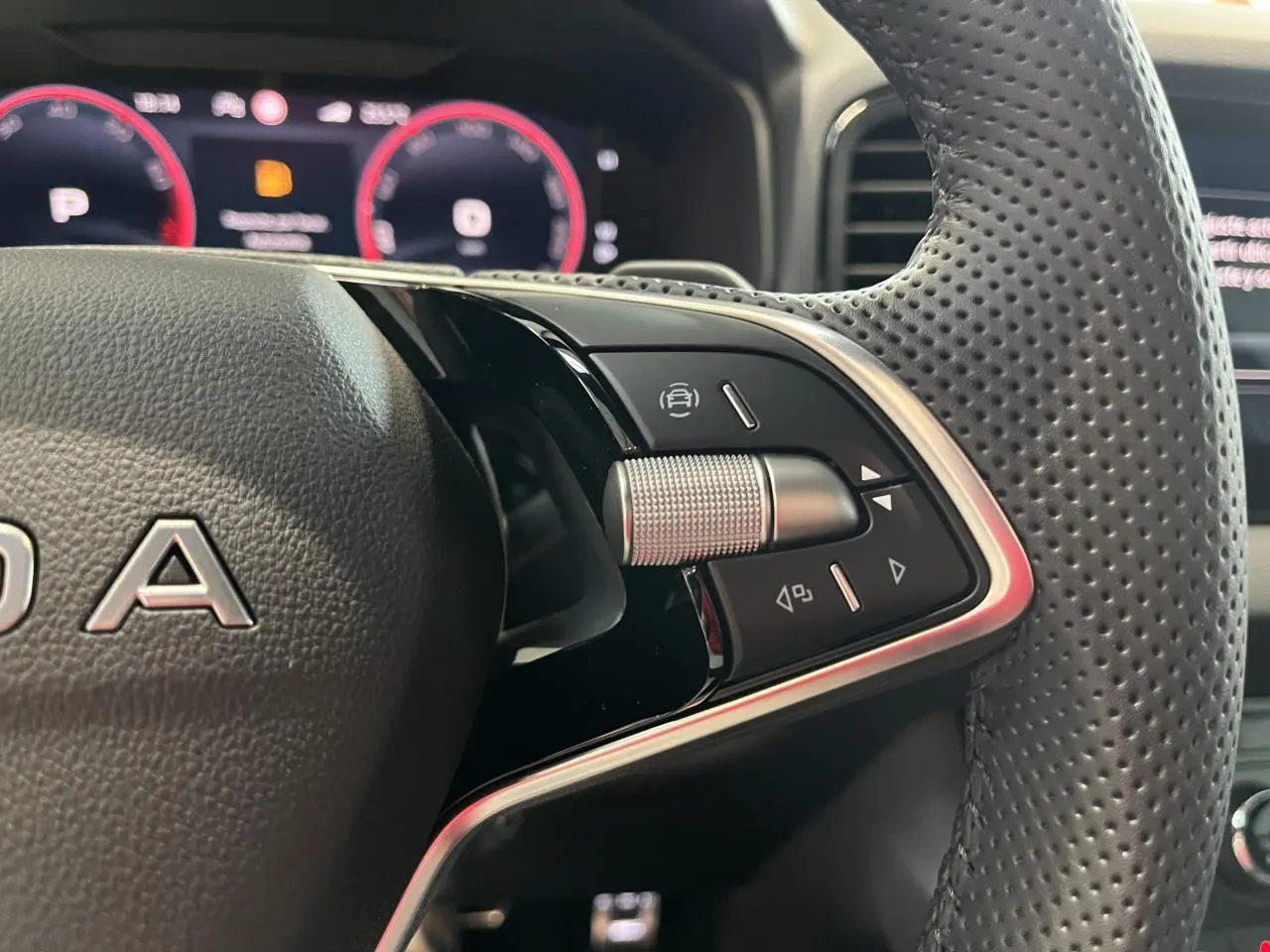 Gros plan sur le volant cuir perforé noir du Skoda Karoq 2025 avec commandes multifonctions et tableau de bord digital rouge.