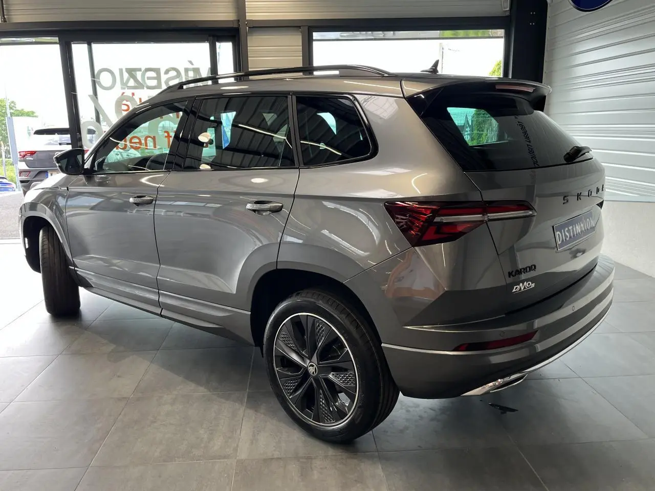 Vue 3/4 arrière droite d'un SUV SKODA KAROQ gris métallisé avec jantes alliage noires et toit noir dans un showroom.