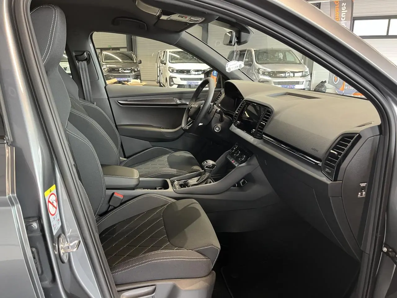 Vue intérieure côté conducteur du Skoda Karoq gris 2025, mettant en valeur les sièges sport noirs et la console centrale moderne.