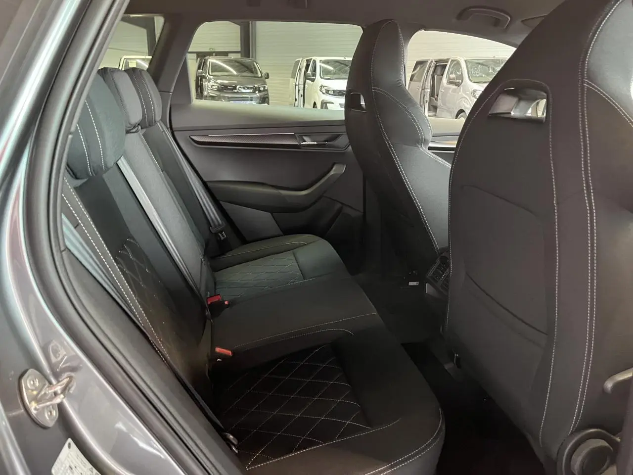 Vue intérieure côté gauche des sièges arrière noirs avec surpiqûres blanches du Skoda Karoq gris 2025 Sportline.