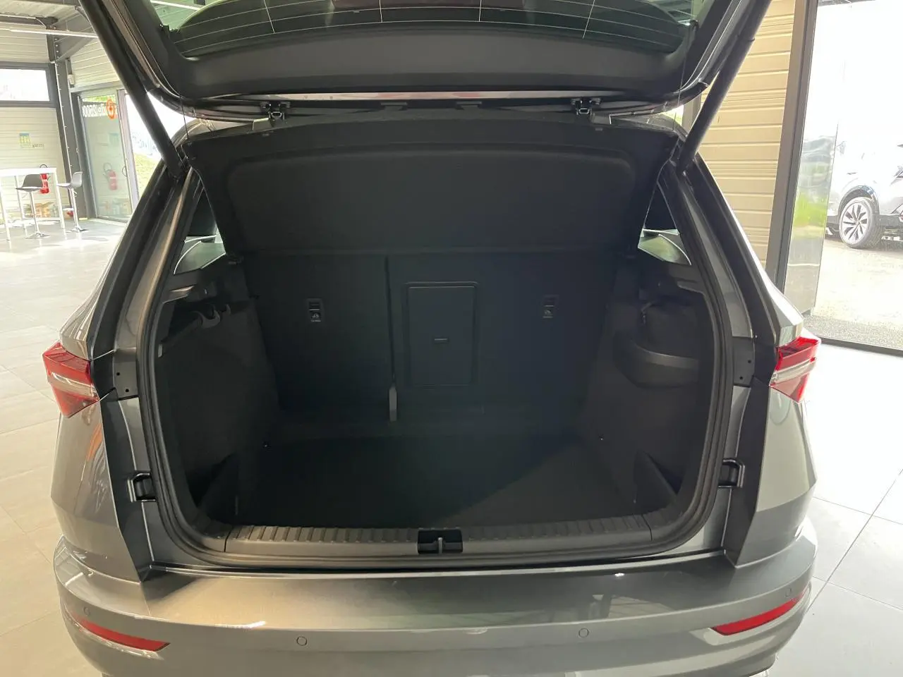 Vue arrière du coffre ouvert d'un SUV SKODA KAROQ gris métallisé 2025 avec hayon électrique et feux LED.
