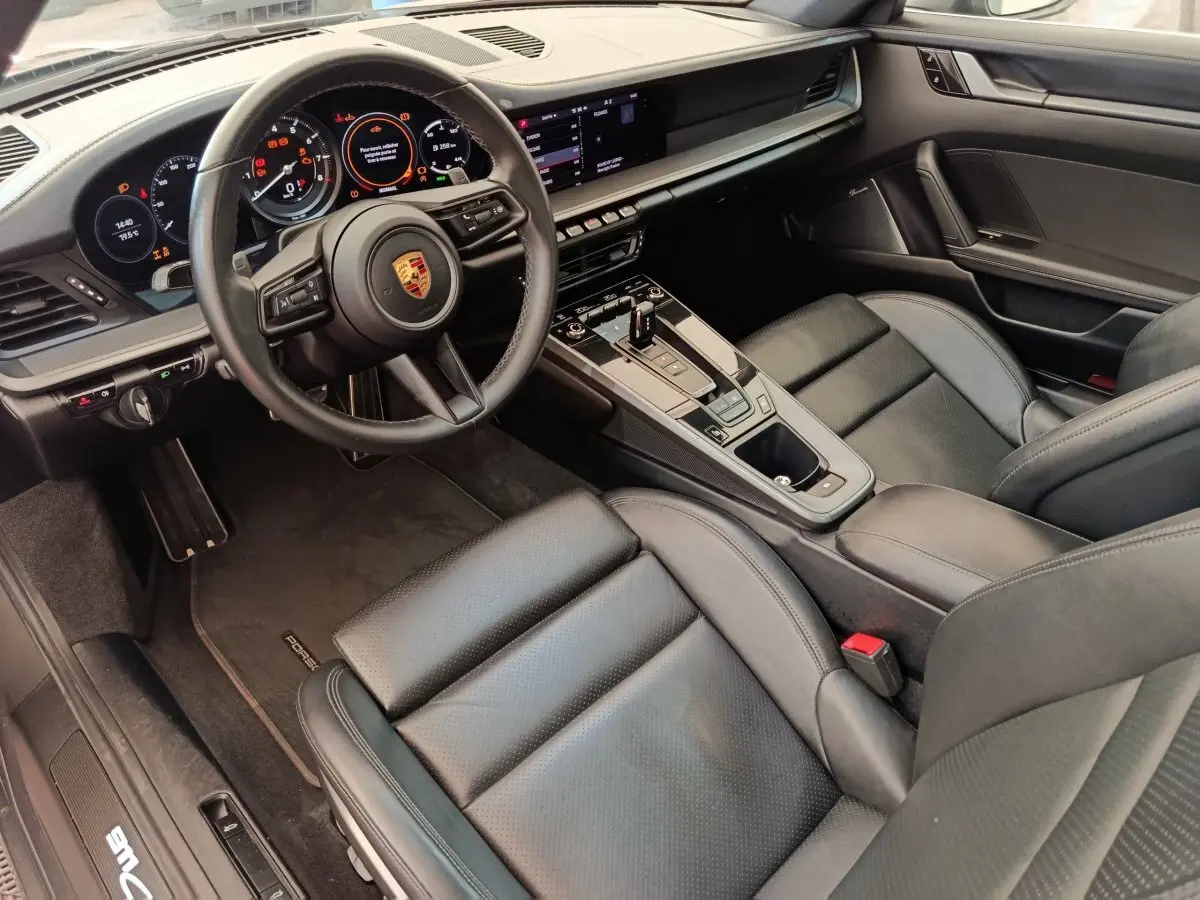 Vue intérieure côté conducteur de la Porsche 911 Carrera 4S 2019, soulignant le tableau de bord digital et les sièges cuir noirs.