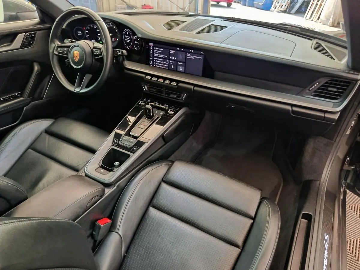 Vue intérieure côté conducteur de la Porsche 911 Carrera 4S Coupé 2019 avec tableau de bord numérique et sellerie cuir noire.