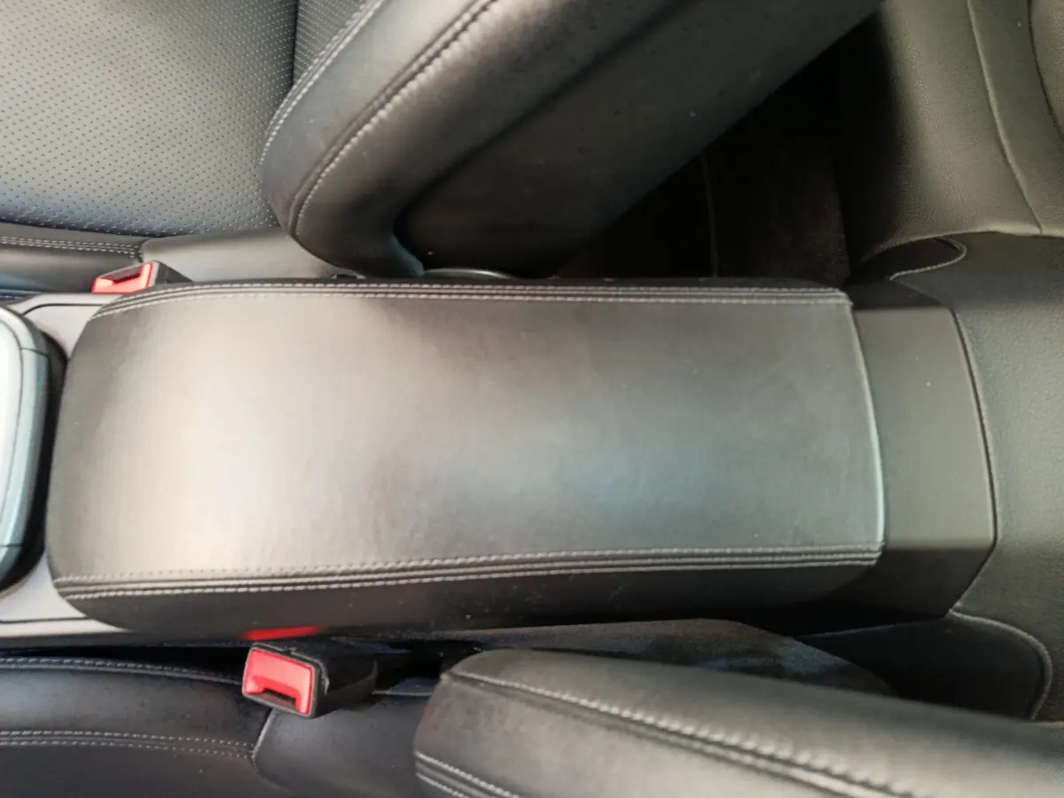 Vue rapprochée de l'accoudoir central en cuir noir et des ceintures de sécurité rouges à l'intérieur d'une Porsche 911 Carrera 4S Coupé gris foncé.