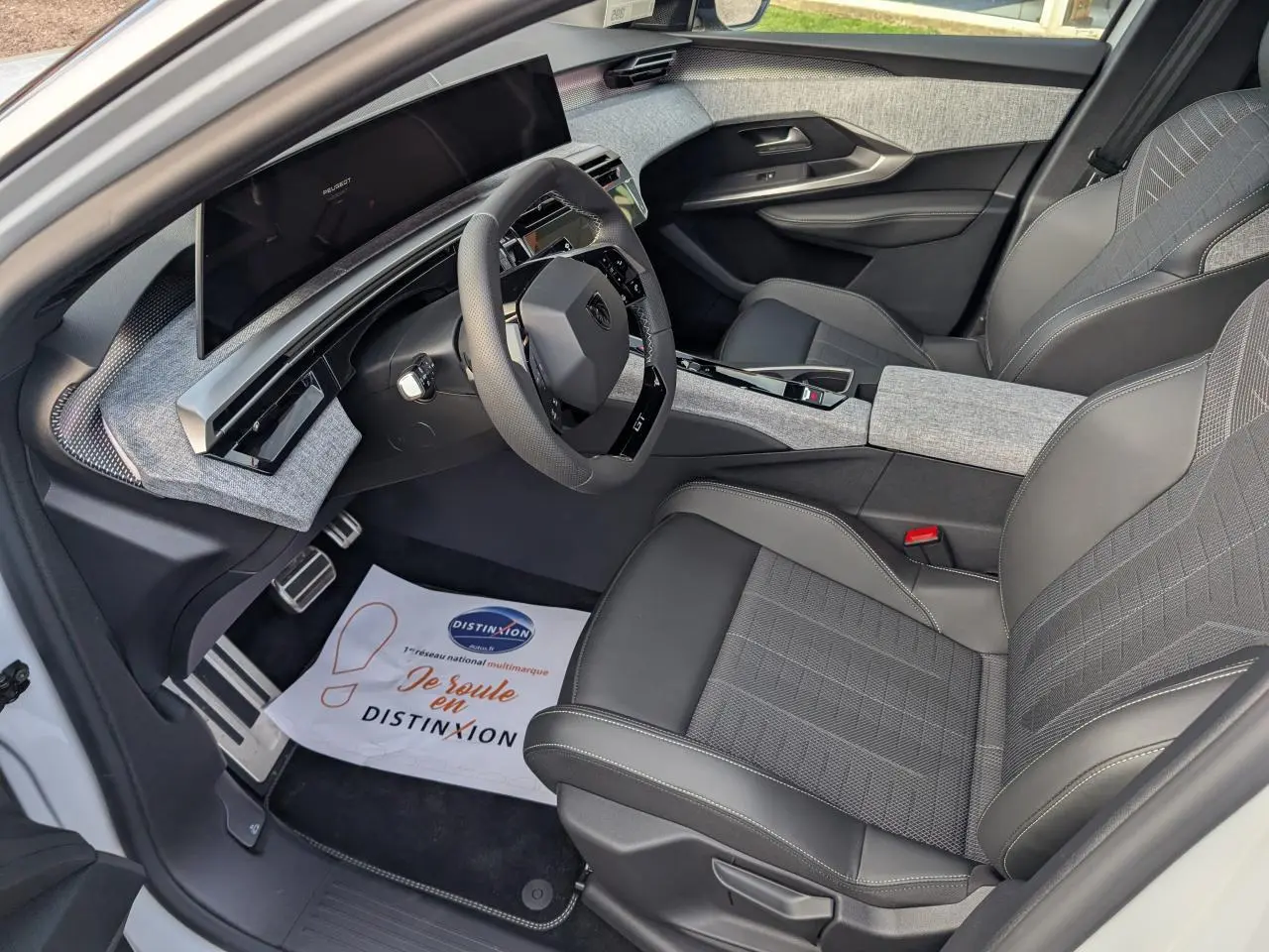 Vue intérieure côté conducteur du Peugeot 3008 GT 2025 blanc, avec sellerie tissu gris et cuir noir, volant compact et tableau de bord numérique.