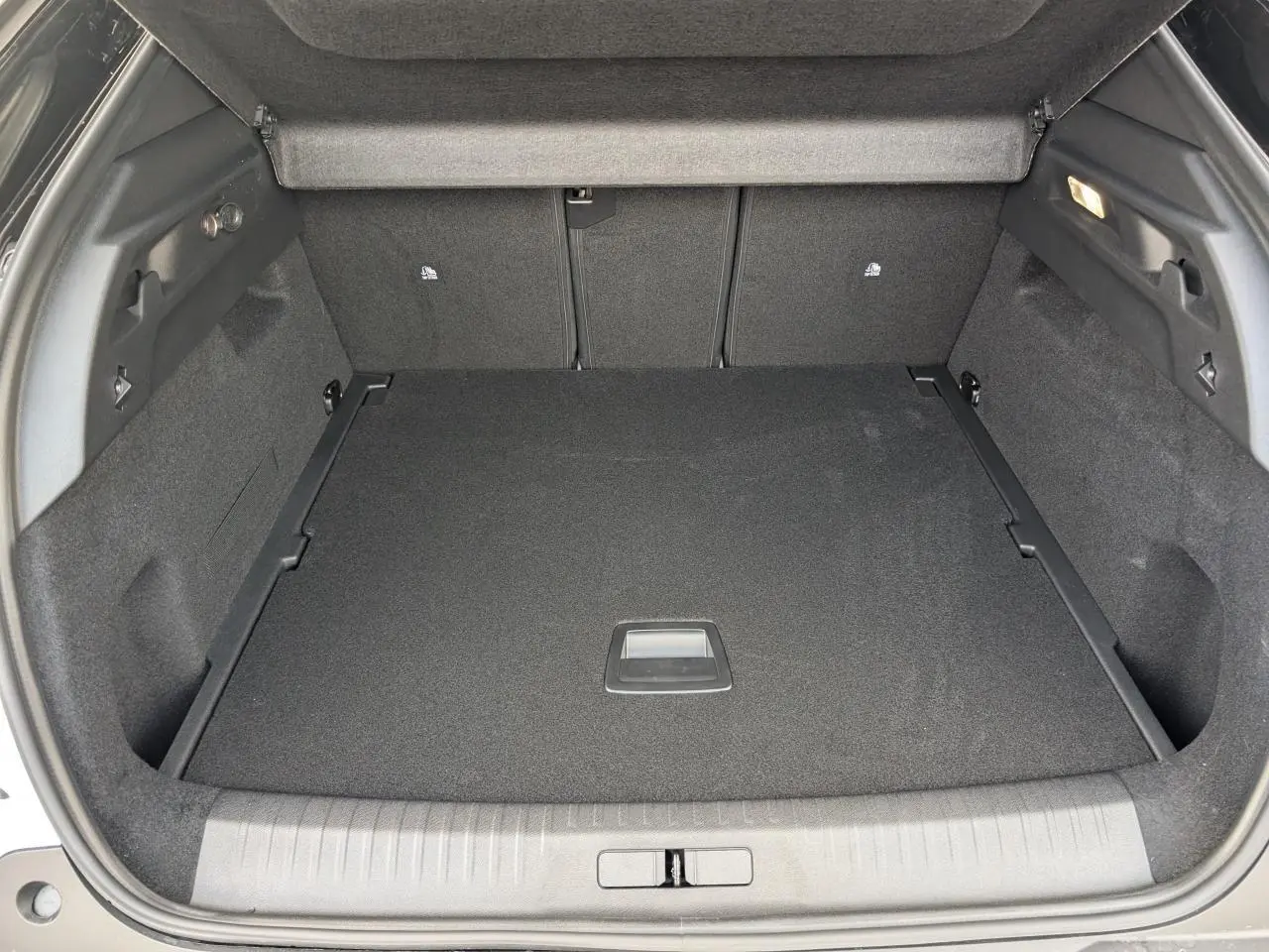Vue plongeante sur le coffre spacieux et noir du Peugeot 3008 blanc, avec habillage intérieur sombre et éclairage latéral.