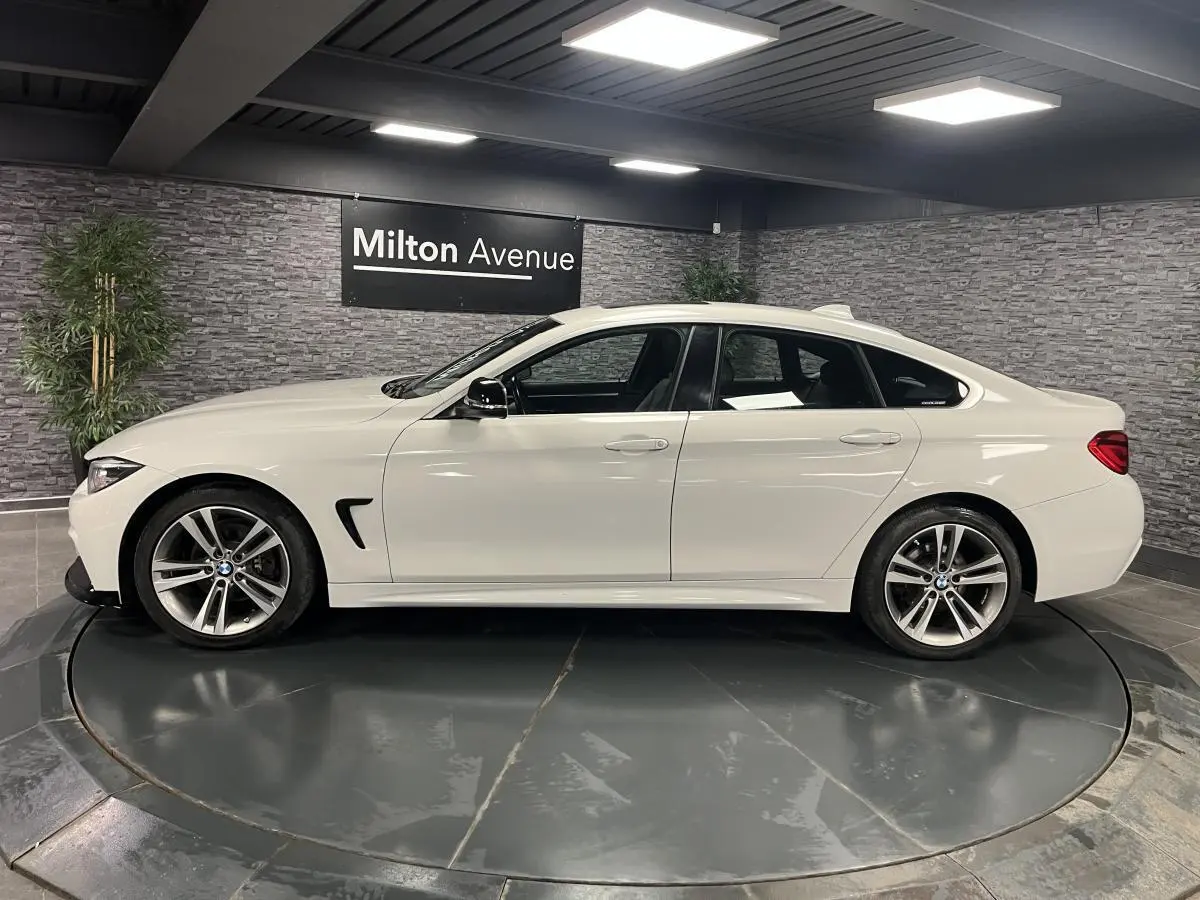 Profil côté gauche d'une BMW Série 4 Gran Coupé blanche avec jantes alliage 18'' en étoile dans un showroom.