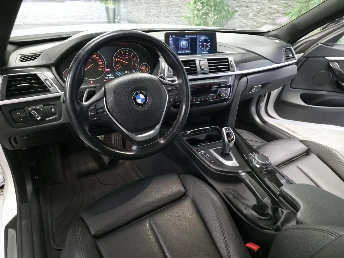 Intérieur BMW Série 4 430i blanc vu côté conducteur, sellerie cuir noire et console centrale avec écran multimédia.