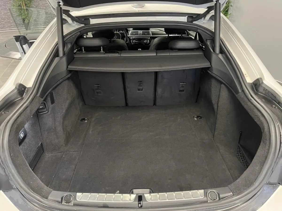 Coffre ouvert d’une BMW Série 4 Gran Coupé blanche, vue intérieure montrant l’espace de chargement et la banquette arrière.