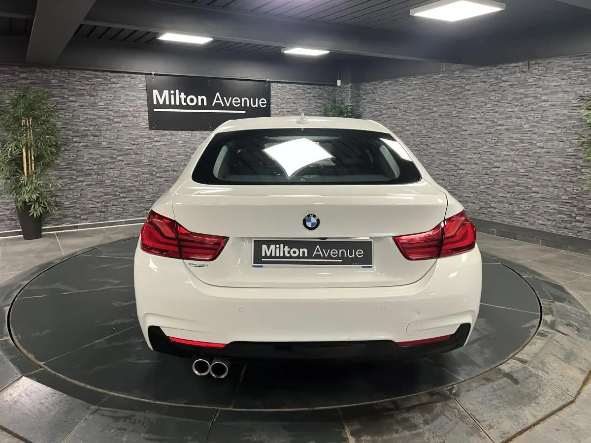Vue arrière d'une BMW Série 4 Gran Coupé blanche avec double sortie d'échappement et feux arrière LED rouges.