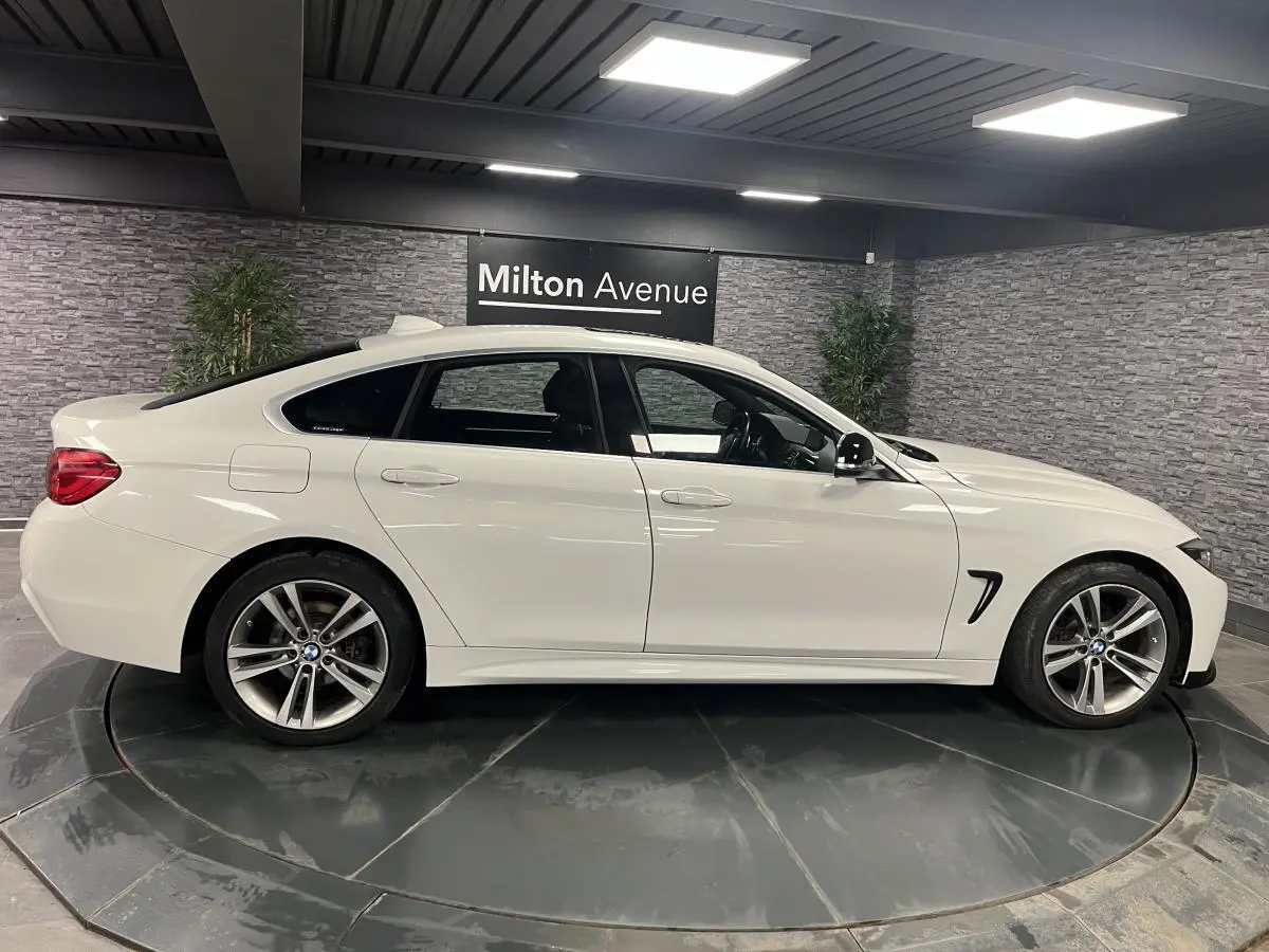 BMW Série 4 430i Gran Coupé blanc vue de profil côté gauche avec jantes alliage 18 pouces en intérieur showroom.